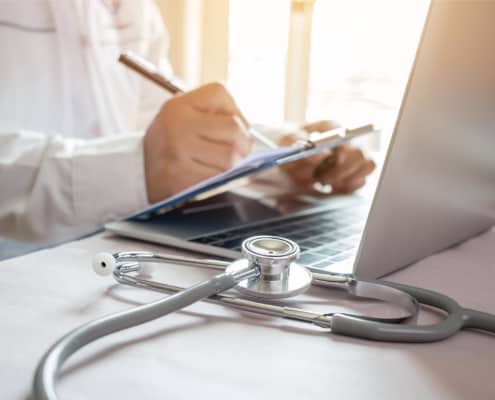 Image of a medical professional using a clipboard and laptop.