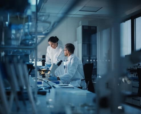 two medical workers assess lab microscope samples in a dimly lit lab