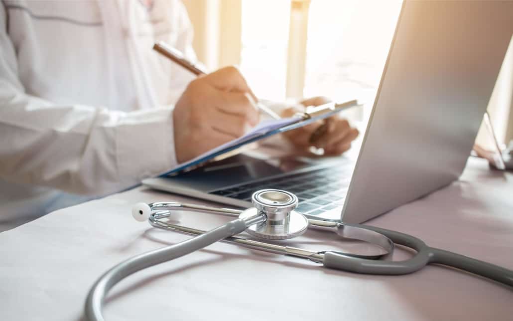 Image of a medical professional using a clipboard and laptop.